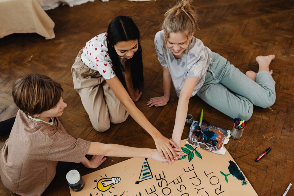 Three teenagers work together on an artistic project indoors, enhancing creativity and teamwork.