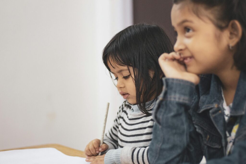 Two young girls joyfully engaged in creative learning indoors, capturing a candid moment of togetherness.
