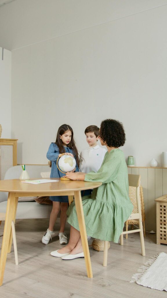 A teacher and two students discussing geography with a globe in a classroom.