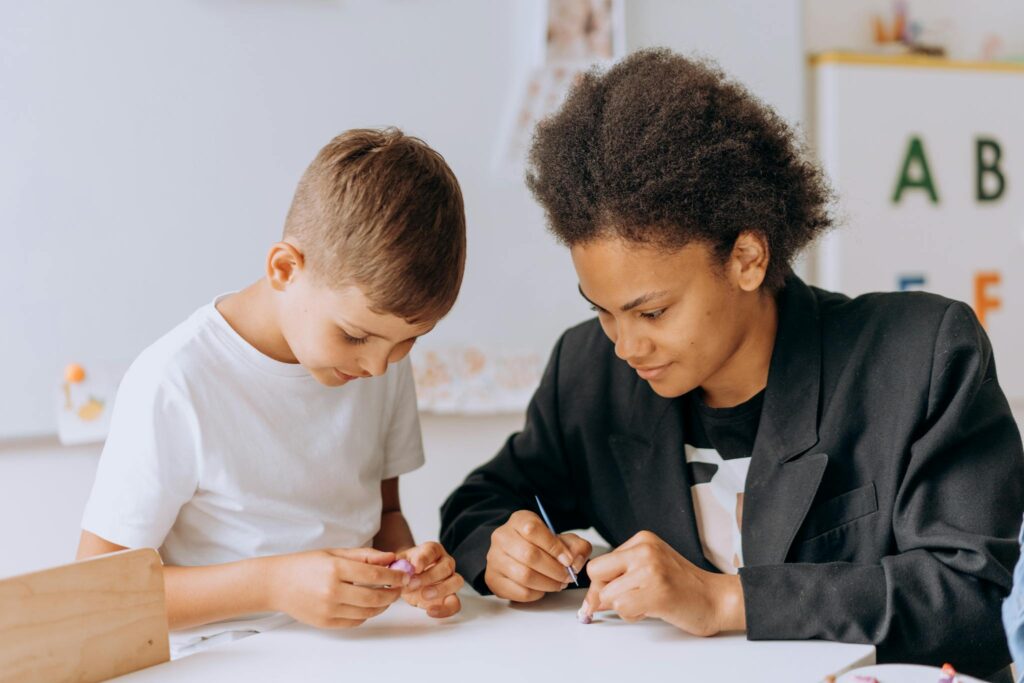A teacher assists a young student with an educational activity in a classroom setting.