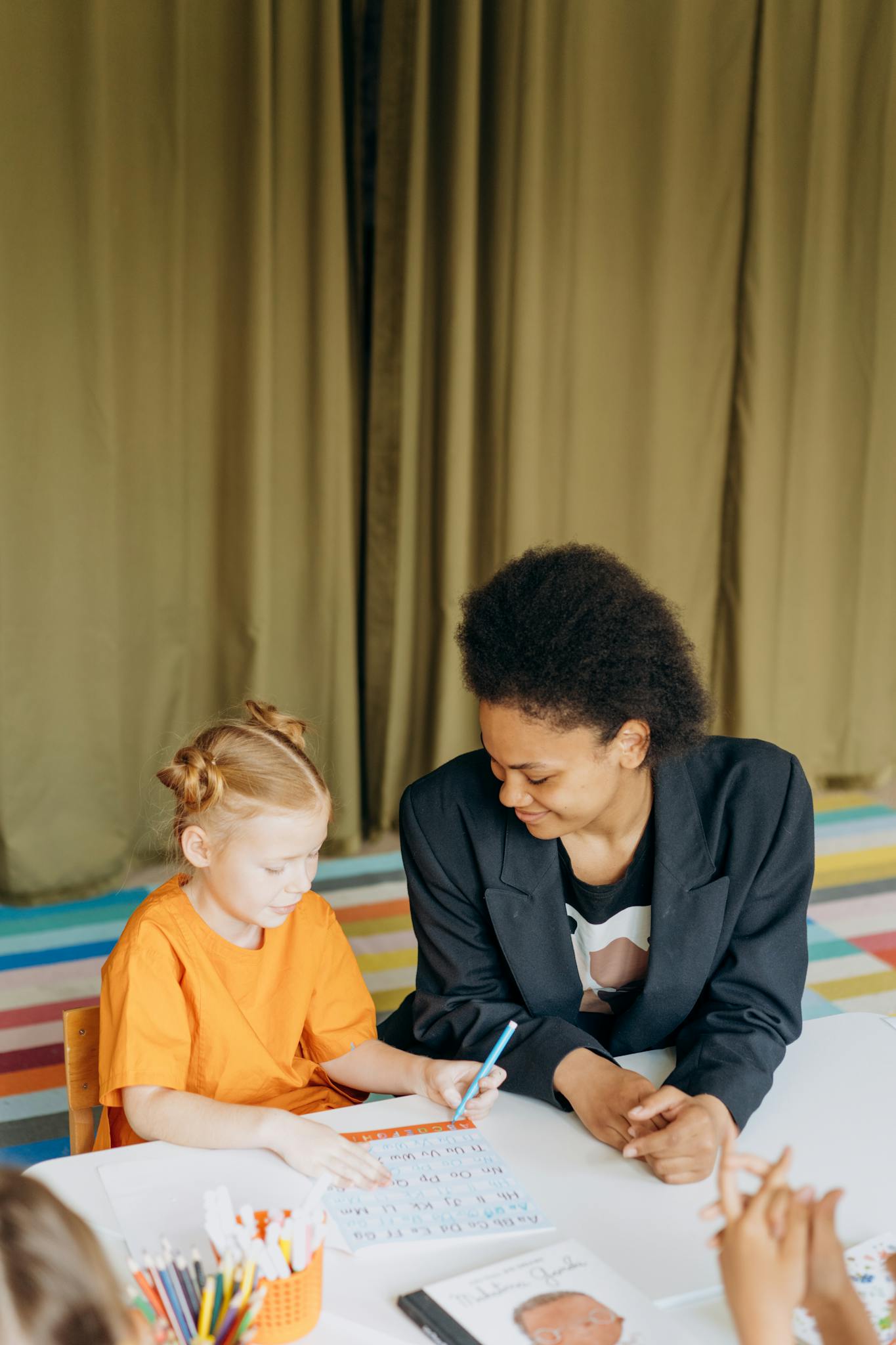 Educator and young girl collaborating on an educational activity in a vibrant classroom setting.