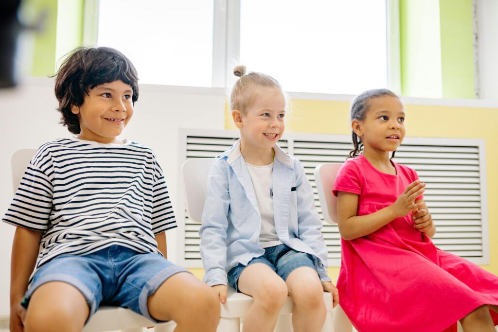 Three happy children sitting together in a bright classroom setting, showcasing friendship and diversity.