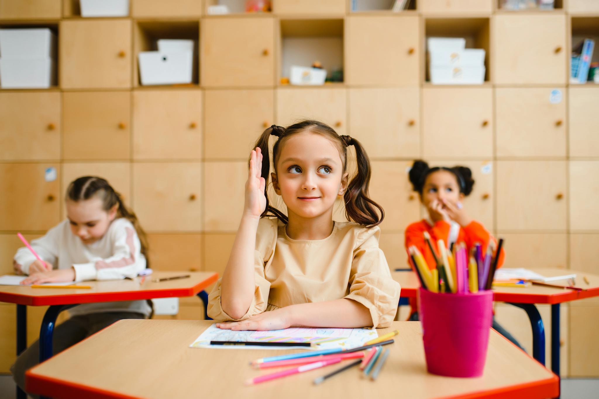 Young girl raises her hand during a lesson in a bright classroom.